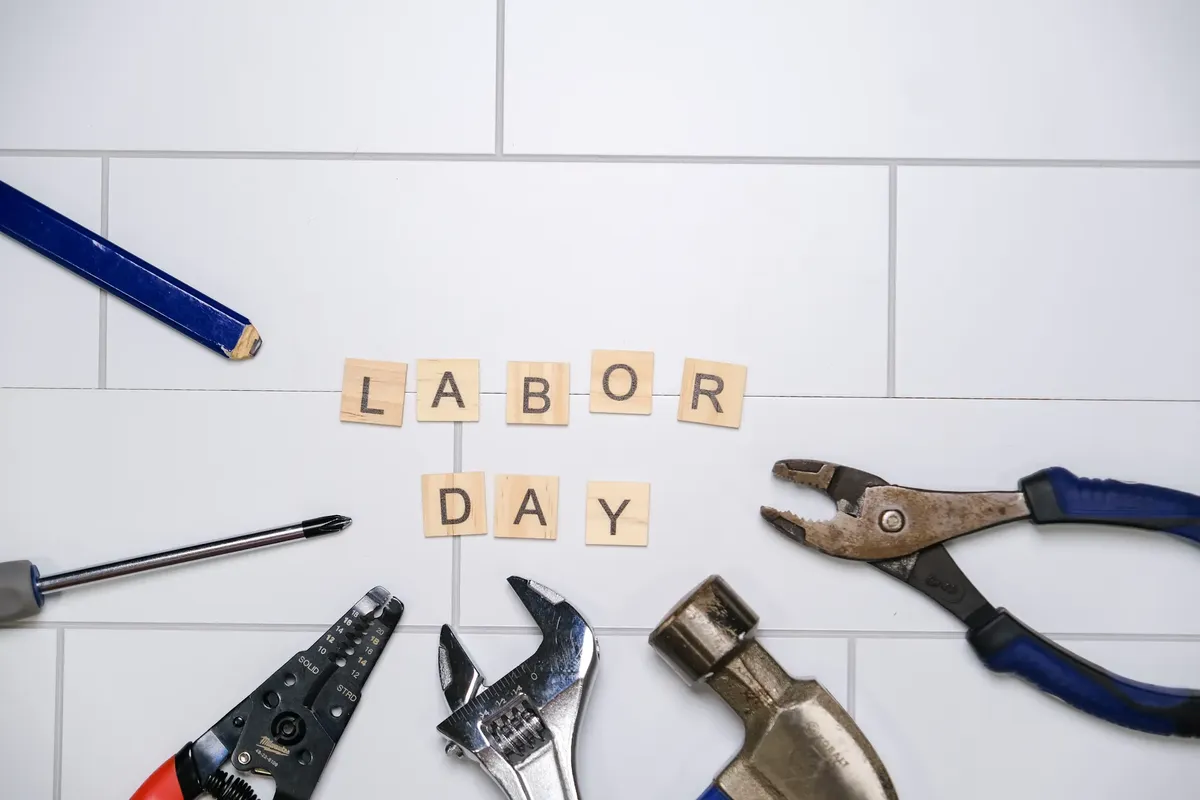 Flat lay of tools and Labor Day text on white tiles, symbolizing construction and work theme.